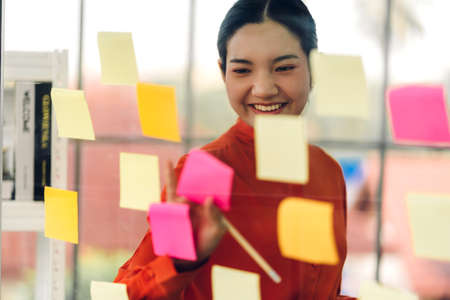 Casual business woman planning and working writing over the project with stickers note on glass window at modern officeの写真素材