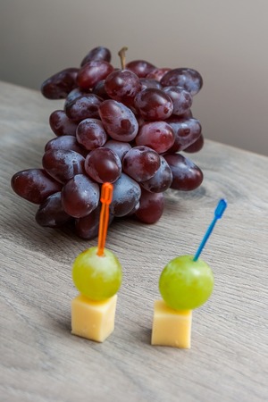 Canape with white grapes and cheese on the background bunch of red grapes, a wooden background.の写真素材