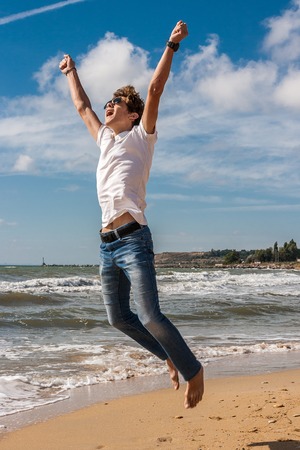 Young man jumping on the beach in the oncoming waves.の写真素材