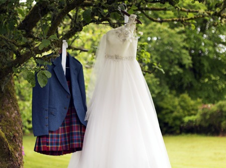 Shot of a Kilt and wedding dress hanging on a treeの写真素材