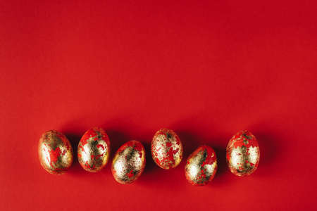 Six golden colored and decorated with sparkles Easter eggs on red background. Happy Easter greeting...