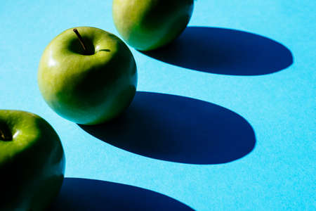 Summer pattern of fresh green apples on blue background under bright sunlight.の写真素材
