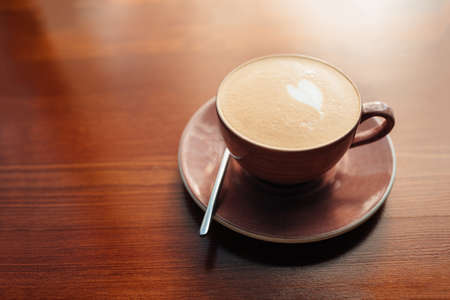 Freshly brewed cappuccino in a cup of faded rose color on a wooden table in the morning during breakfastの写真素材