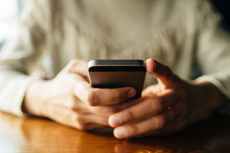 Woman using smartphone on wooden table in cafe. Close-up image with social networks conceptの写真素材