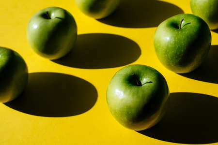 Summer pattern of fresh green apples on yellow background under bright sunlight.の写真素材
