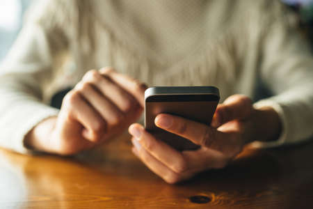 Woman using smartphone on wooden table in cafe. Close-up image with social networks conceptの写真素材