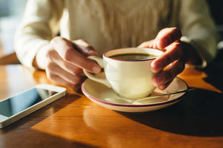 Woman holding in hands cup of coffee on wooden table in cafeの写真素材