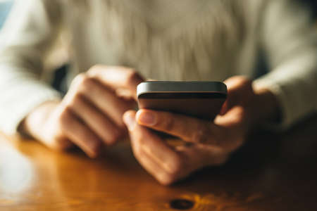 Woman using smartphone on wooden table in cafe. Close-up image with social networks conceptの写真素材