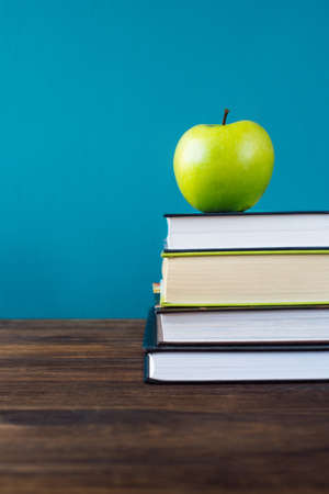School books with apple on desk over school board background