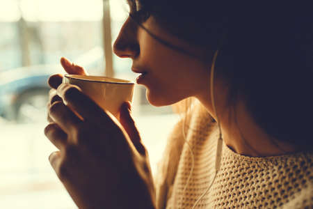 Beautiful girl drinking coffee in a cafe and listening to musicの写真素材