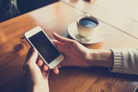 Woman using smartphone on wooden table in cafe. Close-up image with social networks conceptの写真素材