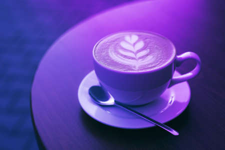Freshly brewed cappuccino in a cup of white color on a wooden table in trendy neon light.の写真素材