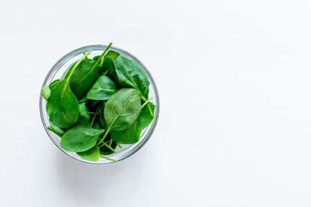 Fresh green spinach leaves in glass bowl on white table. Organic food, healthy diet, vegetarian food. Top view.の写真素材