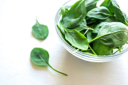 Fresh green spinach leaves in glass bowl on white table. Organic food, healthy diet, vegetarian...