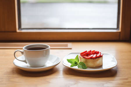 Strawberry tartlet and a cup of tea on wooden table near the window.の写真素材