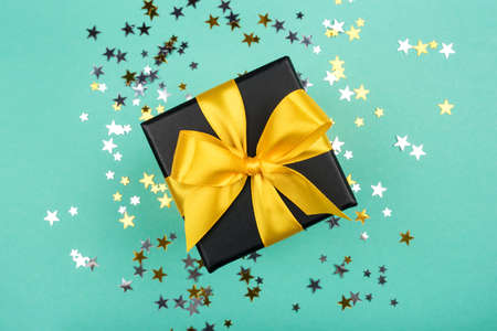 Gift box with yellow bow on green background with sparkling confetti. Flat lay.の写真素材