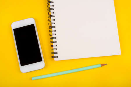 Empty notebook, pencil and phone on yellow background. Flat lay, top view.の写真素材