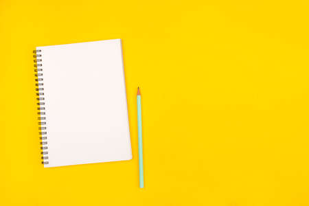 Empty notebook and pencil on yellow background, top view. Copy space.の写真素材