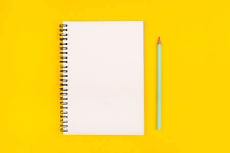 Empty notebook and pencil on yellow background, top view. Copy space.
