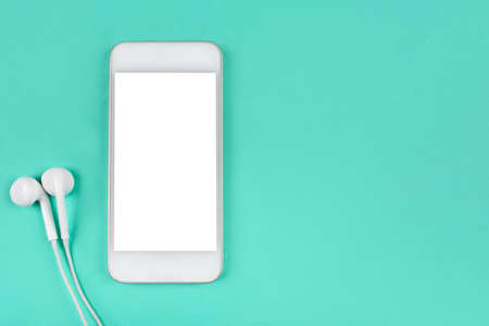 White smartphone with headphones on mint background. Flat lay. Space for your text.の写真素材