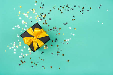 Gift box with yellow bow on green background with sparkling confetti. Flat lay. Copy space.の写真素材