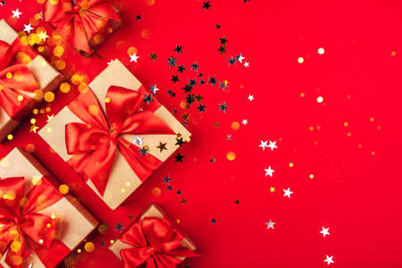 Several gift boxes with bows on a red background with lights and confetti in the shape of stars. Holiday concept.の写真素材