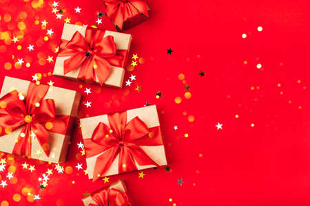 Several gift boxes with bows on a red background with lights and confetti in the shape of stars. Holiday concept.の写真素材