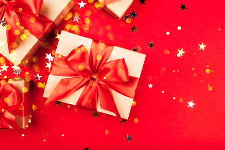 Several gift boxes with bows on a red background with lights and confetti in the shape of stars. Holiday concept.の写真素材