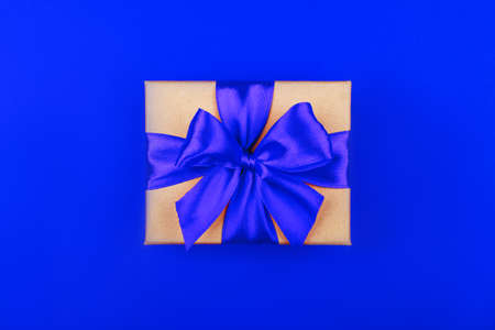 Cardboard gift box with bow on blue background. Flat lay. Top view. Color of year 2020.の写真素材