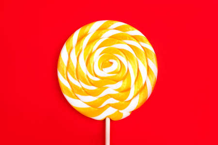 Yellow lollipop in the shape of a circle on a red background. Flat lay, top view.