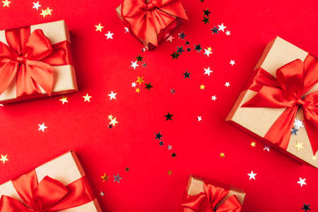 Several gift boxes with bows on a red background with confetti in the shape of stars. Holiday concept.の写真素材
