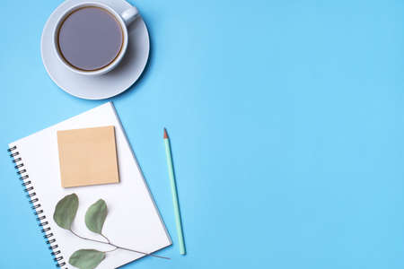 Blue background with notepad, pencil and cup of coffee. Top view with copy space, flat lay.