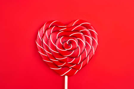 A heart-shaped lollipop on a red background. Valentine's Day concept. Flat lay, top view.の写真素材