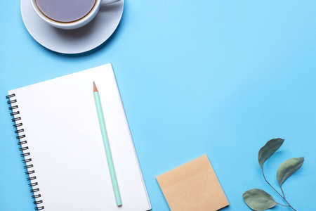 Blue background with notepad, pencil and cup of coffee. Top view with copy space, flat lay.