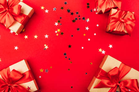 Several gift boxes with bows on a red background with confetti in the shape of stars. Holiday concept.の写真素材