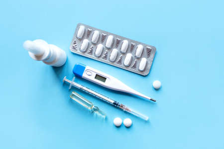 Digital thermometer and medicaments on blue background. Treatment concept. Flat lay, top view.