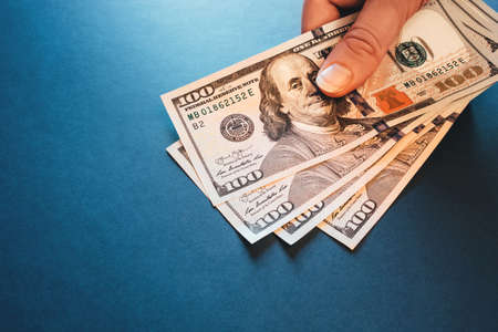 American cash dollars. Hundred-dollar bills in hand on blue background.