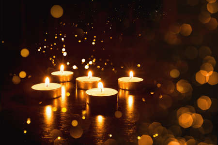 Several burning candles with festive bokeh on a black background.の写真素材
