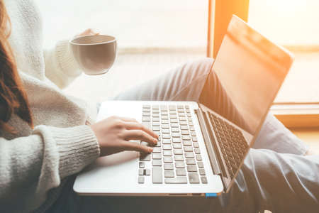 A young woman reads the news at home on her laptop and drinks coffee.の写真素材