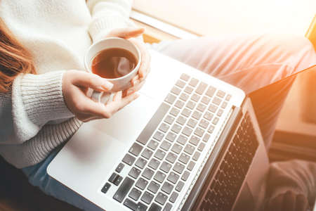 A young woman reads the news at home on her laptop and drinks coffee.の写真素材