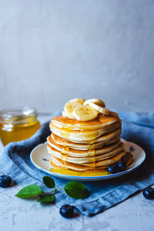 A stack of pancakes with fresh banana, blueberry and honey. Delicious homemade breakfast.の写真素材