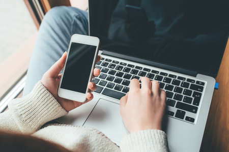 Young woman working in a home office on her laptop and smartphone. Remote work concept.の写真素材