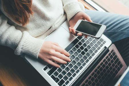 Young woman working in a home office on her laptop and smartphone. Remote work concept.の写真素材