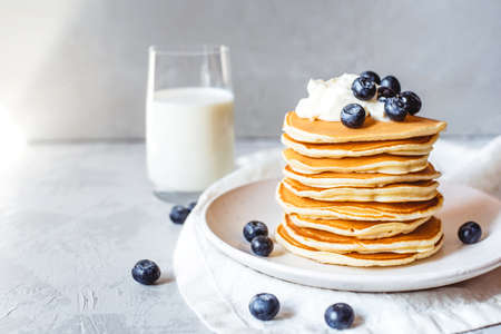 A stack of pancakes with fresh blueberries, cheese cream and glass of milk. Delicious homemade breakfast.の写真素材