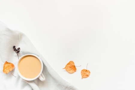 Autumn background. A cup of hot coffee or tea with milk on white wooden background with autumn leaves, napkin and cones. Copy space for text. Flat lay, top view.の写真素材