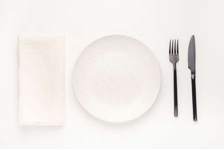 Set of black cutlery knife and fork, white plate and napkin on a white wooden table. Restaurant or cafe concept.の写真素材