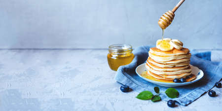 A stack of pancakes with fresh banana, blueberry and honey. Delicious homemade breakfast. Banner with copy space for text.の写真素材