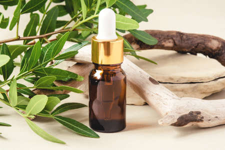 Brown bottle with cosmetic product on a natural beige background made of branches and green leaves.の写真素材