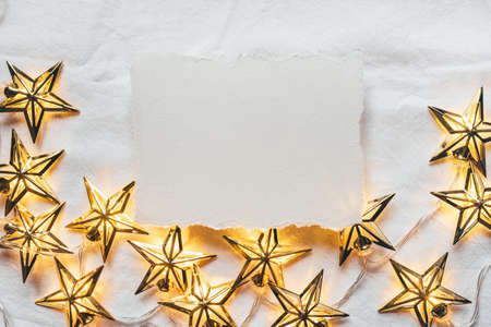 Greeting card for Christmas or New year of golden garlands in the shape of stars with a paper card-note. Flat lay. Minimal concept.の写真素材