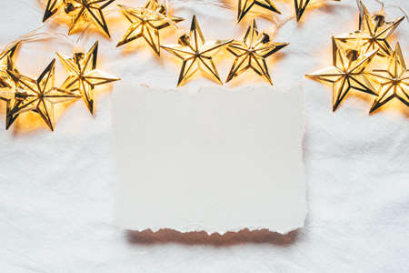 Greeting card for Christmas or New year of golden garlands in the shape of stars with a paper card-note. Flat lay. Minimal concept.の写真素材